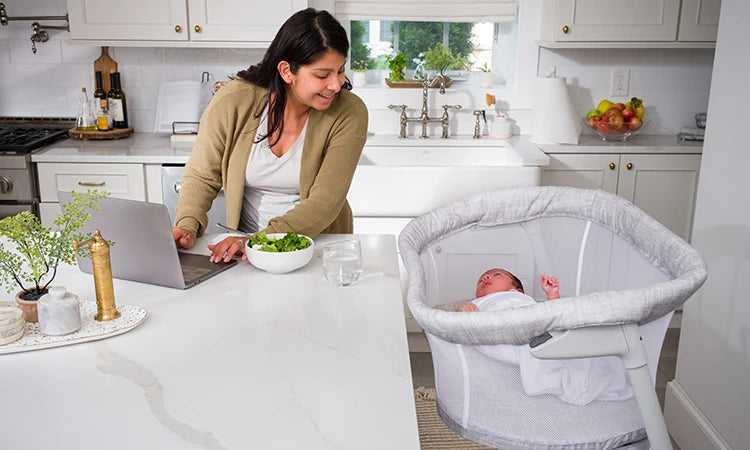 Mother in Kitchen with Baby in a BassiNest Flex Bassinet Heather Weave